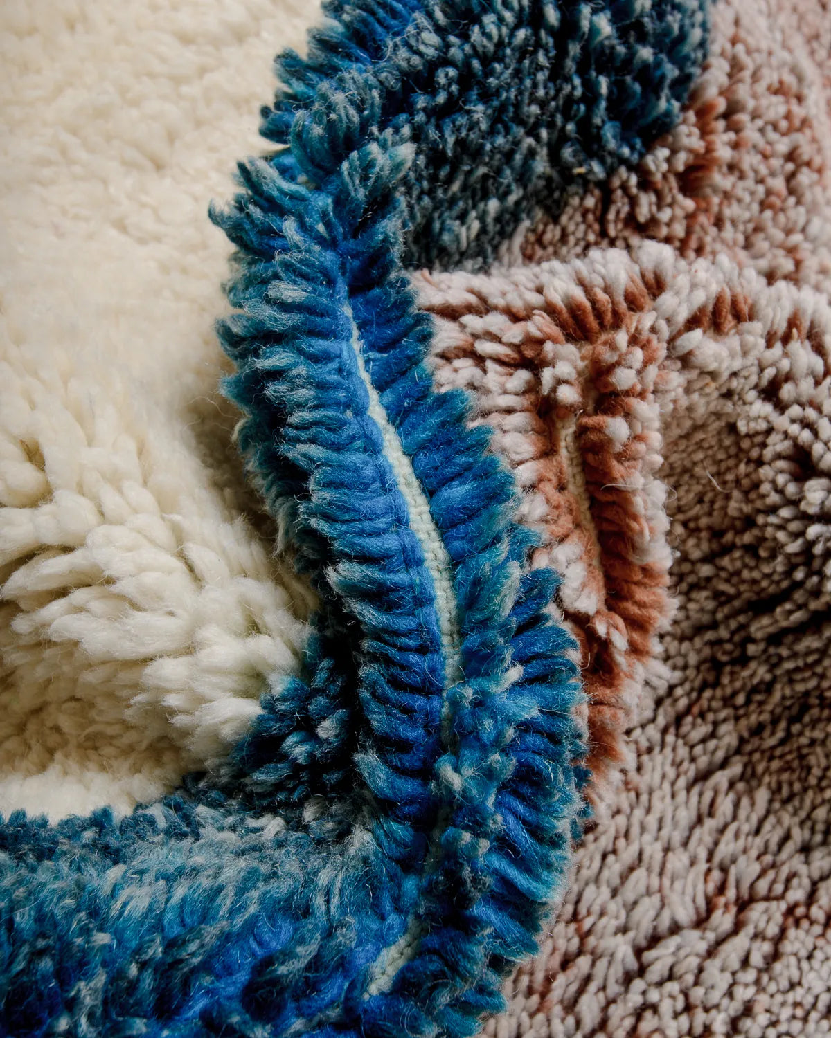 Detail of fluffy wool rug in petrol, cream and mottled lavender-rust.